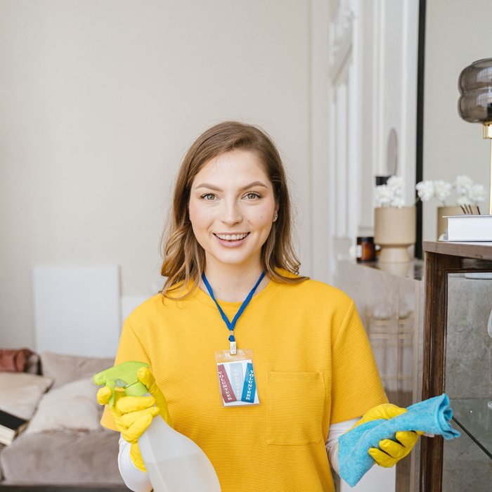 Smiling cleaner holding cleaning spray and gloves
