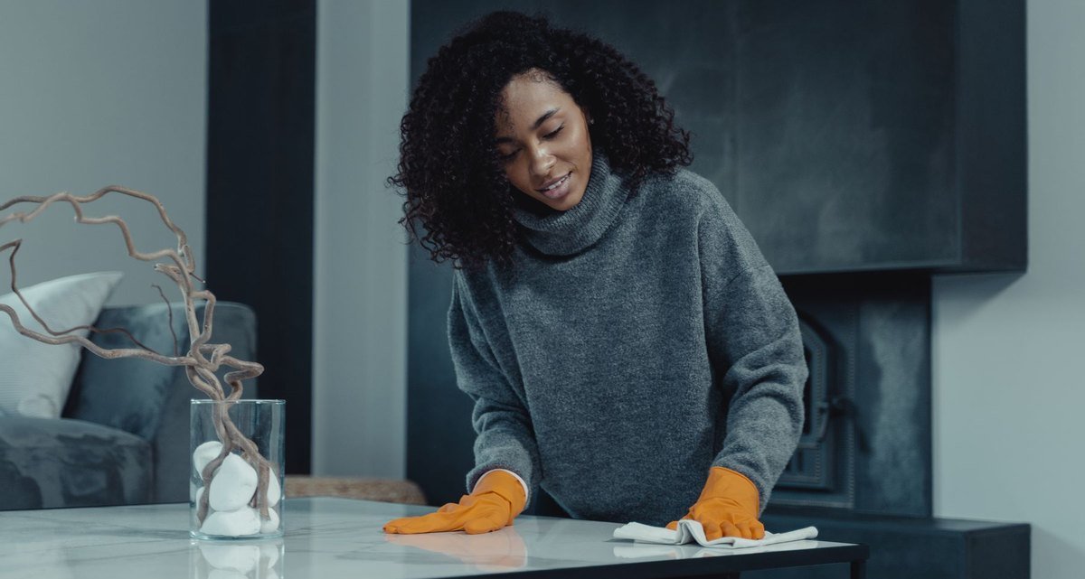 Cleaner wiping a table with orange gloves in a living room