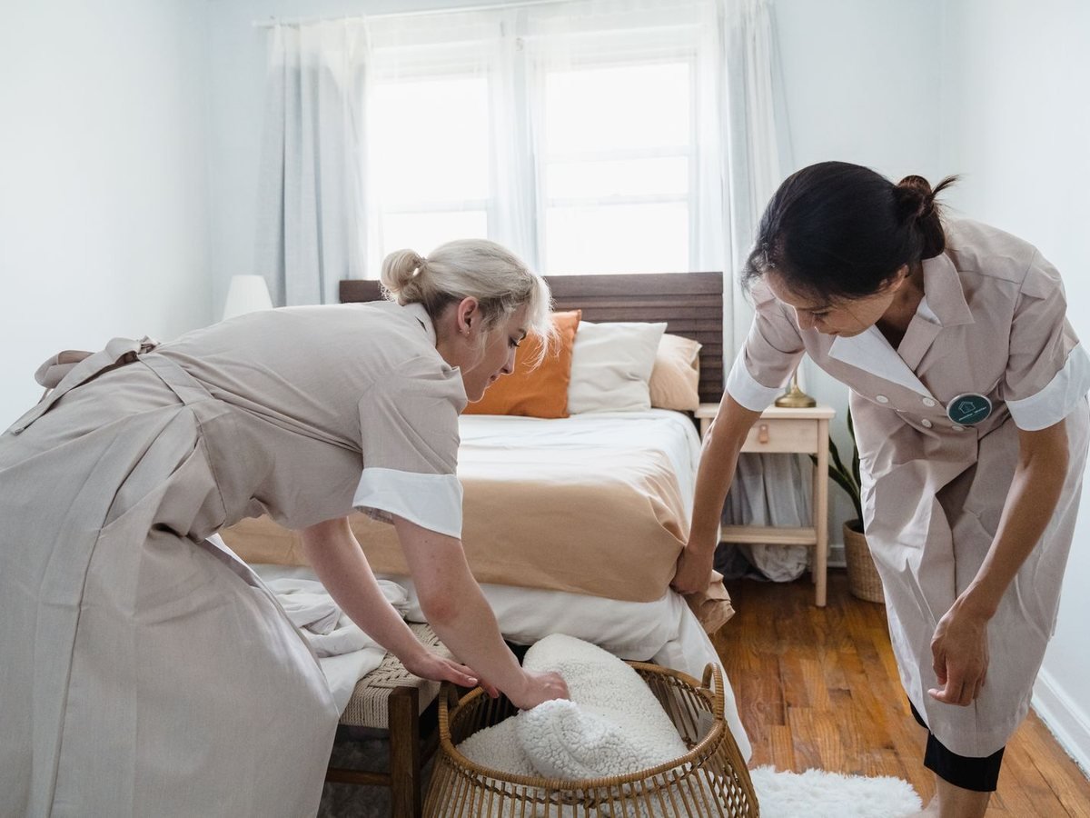 Two housekeepers making up a bed with fresh linen