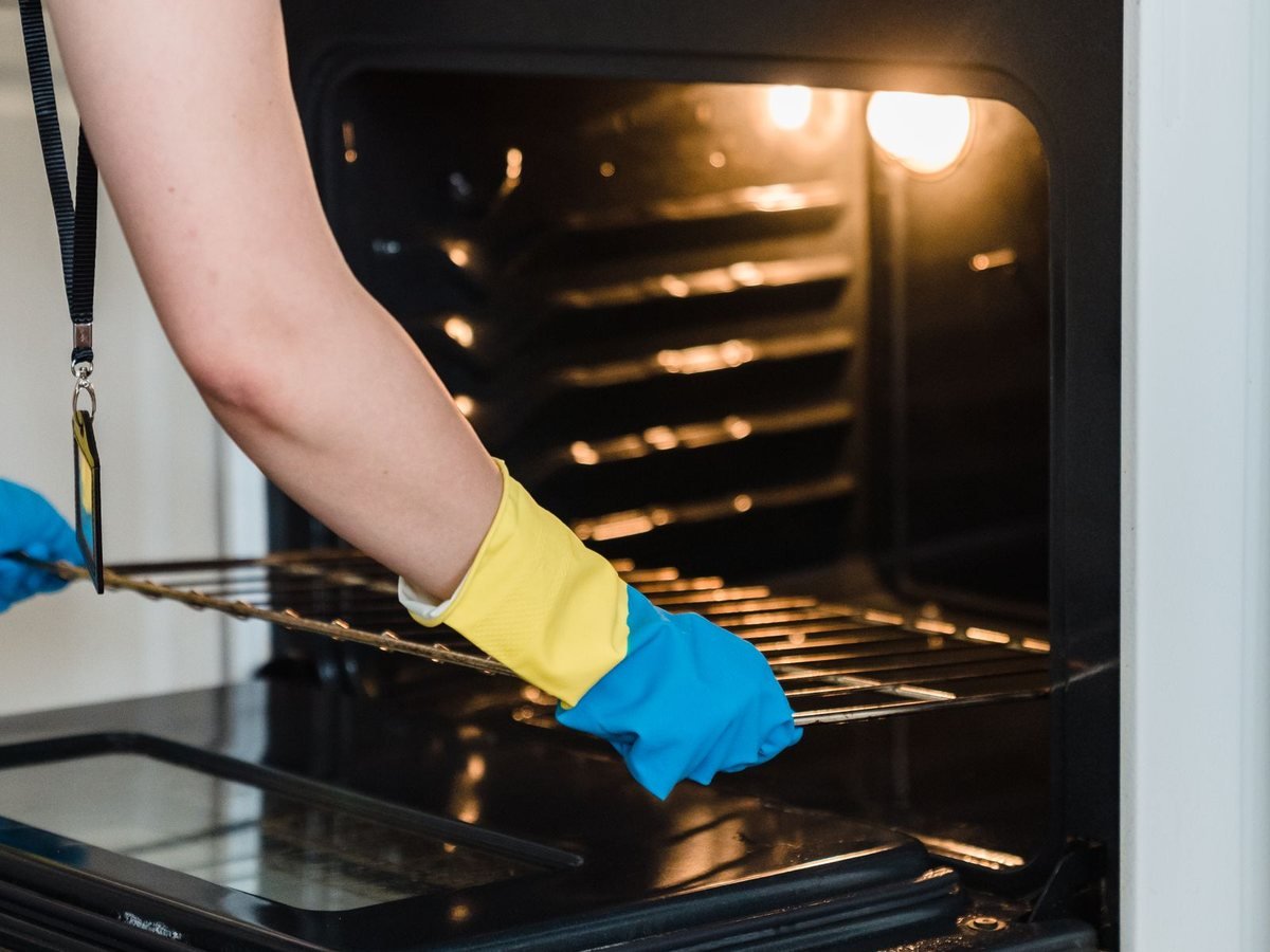 Cleaner in gloves scrubbing an oven